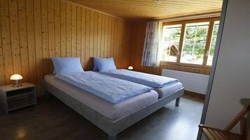 Une chambre avec deux lits, des murs en bois, une fenêtre donnant sur un beau paysage et une table de chevet avec une lampe.
