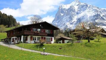 Un bâtiment de style chalet, avec une façade en bois, un balcon et une vue sur une montagne enneigée.