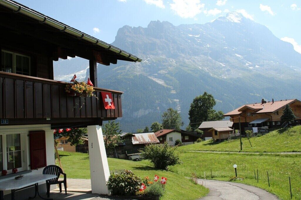 Un chalet doté d’un balcon, décoré aux couleurs du drapeau suisse, et offrant une vue sur la montagne.