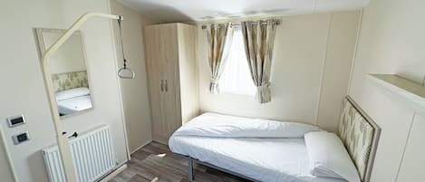 Een kleine, goed verlichte kamer met een bed, een radiator, een spiegel en een kledingkast.