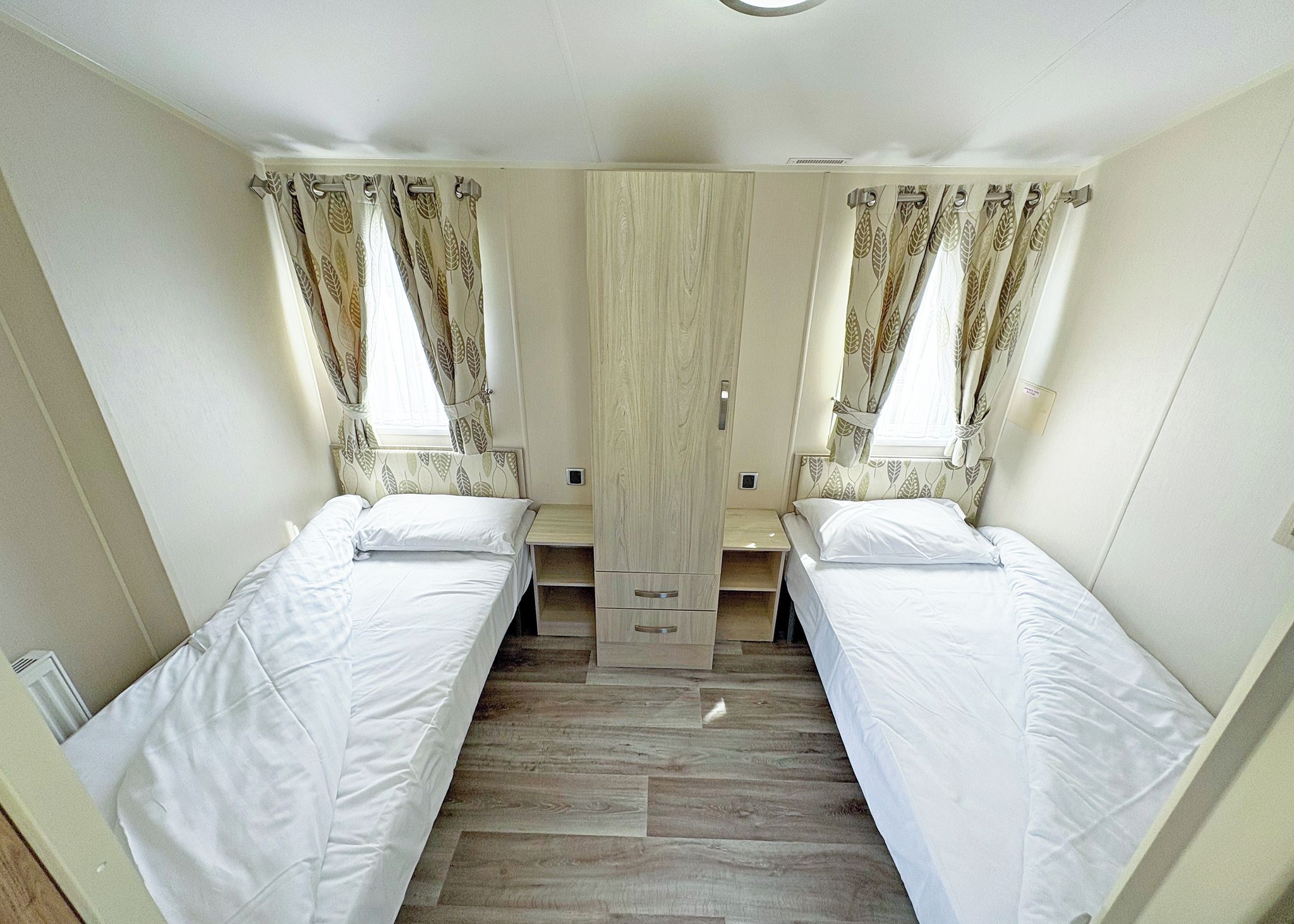 A compact room with two single beds, a wardrobe, and curtains.