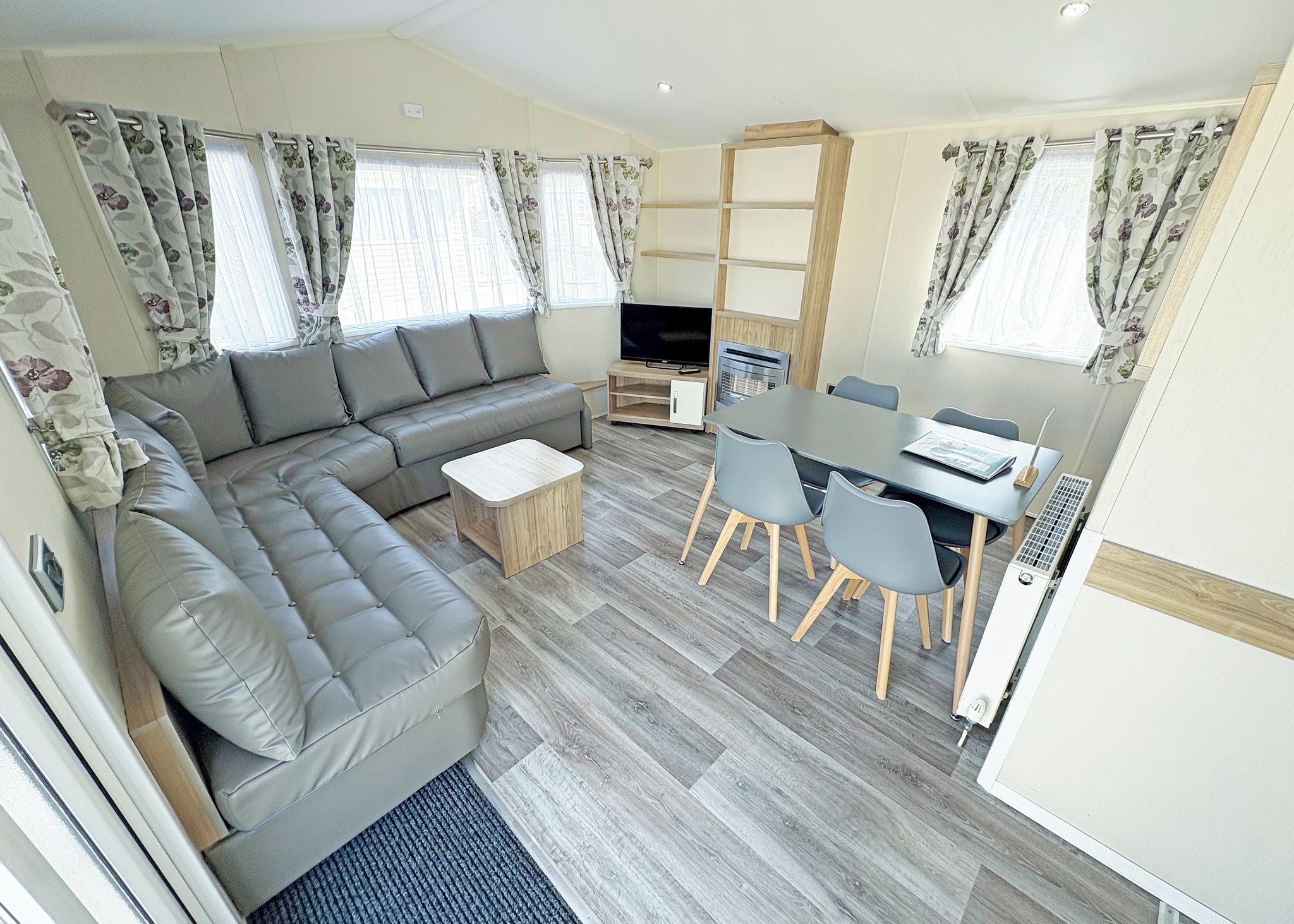 A modern living area with a sectional sofa, a small coffee table, a dining table with chairs, and a TV.