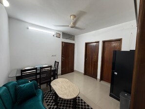 Una sala de estar con sofá, una mesa de comedor, sillas, un ventilador de techo y un refrigerador negro.