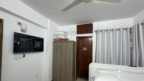 Een slaapkamer met een bed, een plafondventilator, een kledingkast, een aan de muur bevestigde televisie en een deur.