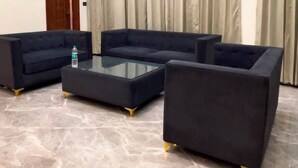A room with a sectional sofa set, a glass coffee table, and a marble floor.