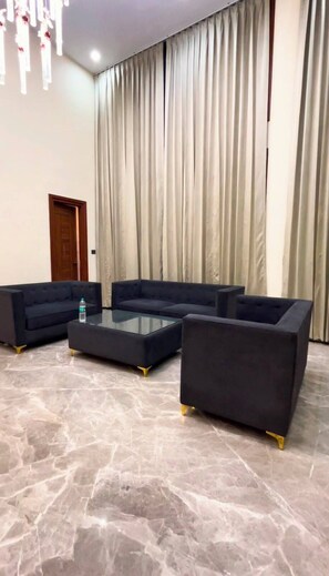 A room with a sectional sofa set, a glass coffee table, and a marble floor.