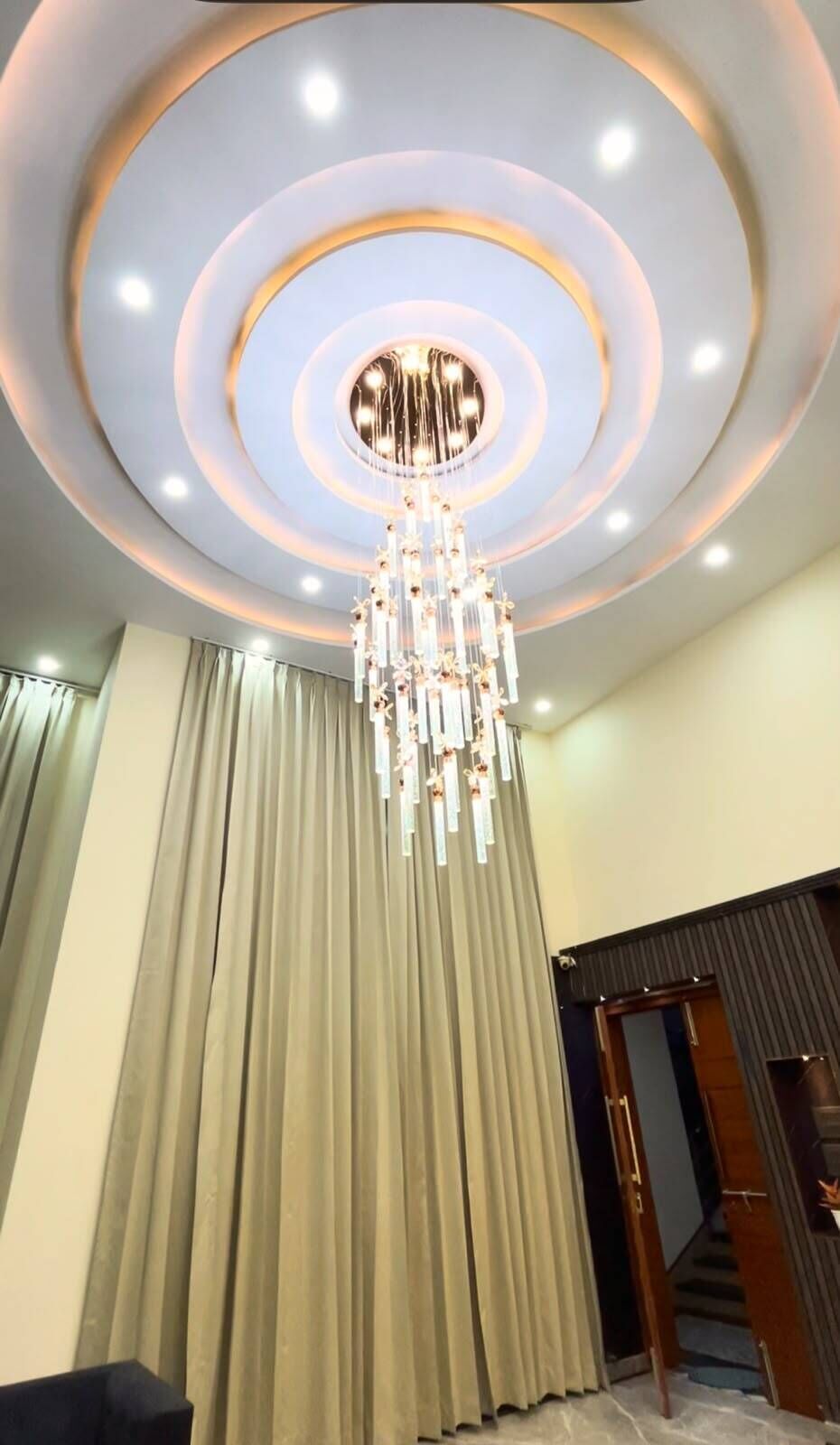 A room with a chandelier, curtains, and a staircase.