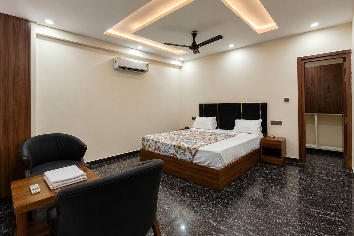 Ein modernes Hotelzimmer mit Bett, Sessel, Nachttisch, Klimaanlage und Deckenventilator.