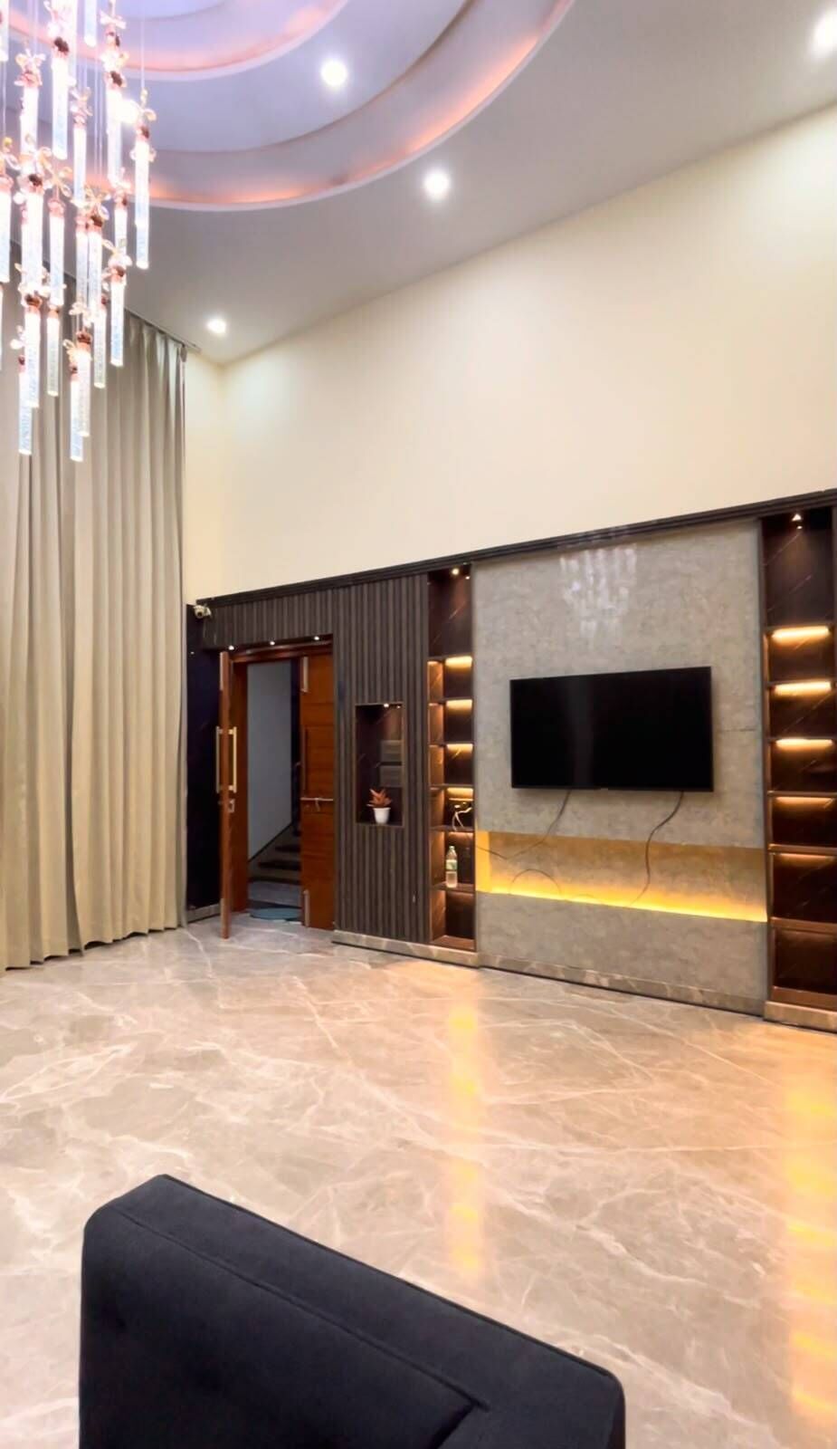 A modern lobby with a flat-screen TV mounted on a wall, a staircase leading to another level, and a chandelier.