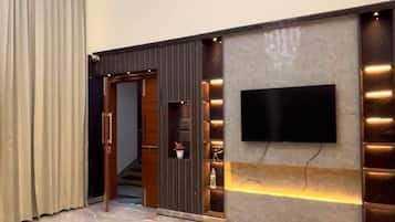 A modern lobby with a flat-screen TV mounted on a wall, a staircase leading to another level, and a chandelier.