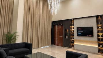 A modern lobby with a chandelier, sofas, a TV, and a plant.