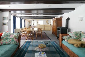 Ein Wohnzimmer mit Glastisch, Korbmöbeln und Blick zur Küche.