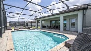 A swimming pool with a glass enclosure, lounge chairs, and a patio area with a table and chairs.