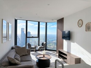 Ein modernes Wohnzimmer mit Sofa, Couchtisch, Fernseher und großen Fenstern mit Blick auf die Stadt.