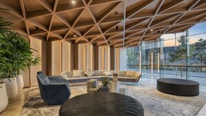 A modern interior with a geometric ceiling, a sofa set, a round black ottoman, and large windows. - New luxury 51st Floor skyline sunshine view (Southbank)