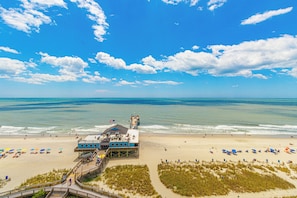 Ein Gebäude am Strand mit einem Steg, Strandsonnenschirmen und freiem Blick auf den Ozean.