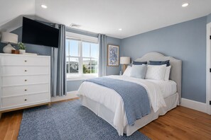 A bedroom with a bed, a dresser, a TV, a window, and a painting.