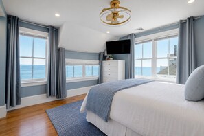 Un dormitorio con una cama grande, ventilador de techo, televisor y vista al mar.