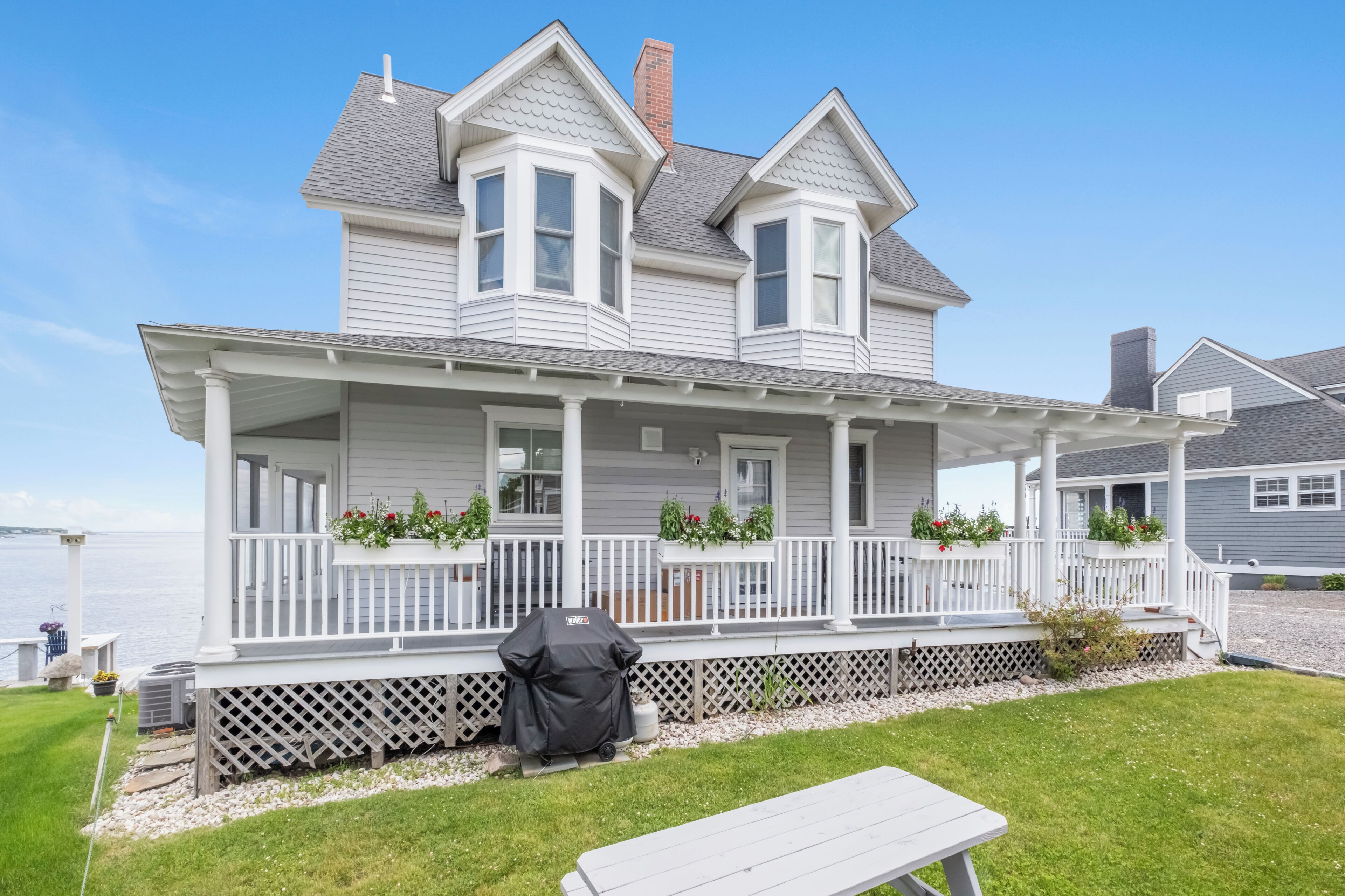 A two-story house with a covered porch, a grill, and a picnic table.