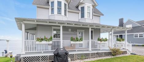 A two-story house with a covered porch, a grill, and a picnic table.