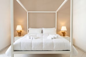 Ein Bett mit Baldachin, ausgestattet mit weißer Bettwäsche, zwei Nachttische mit Lampen und eine Wand in neutralen Farben.