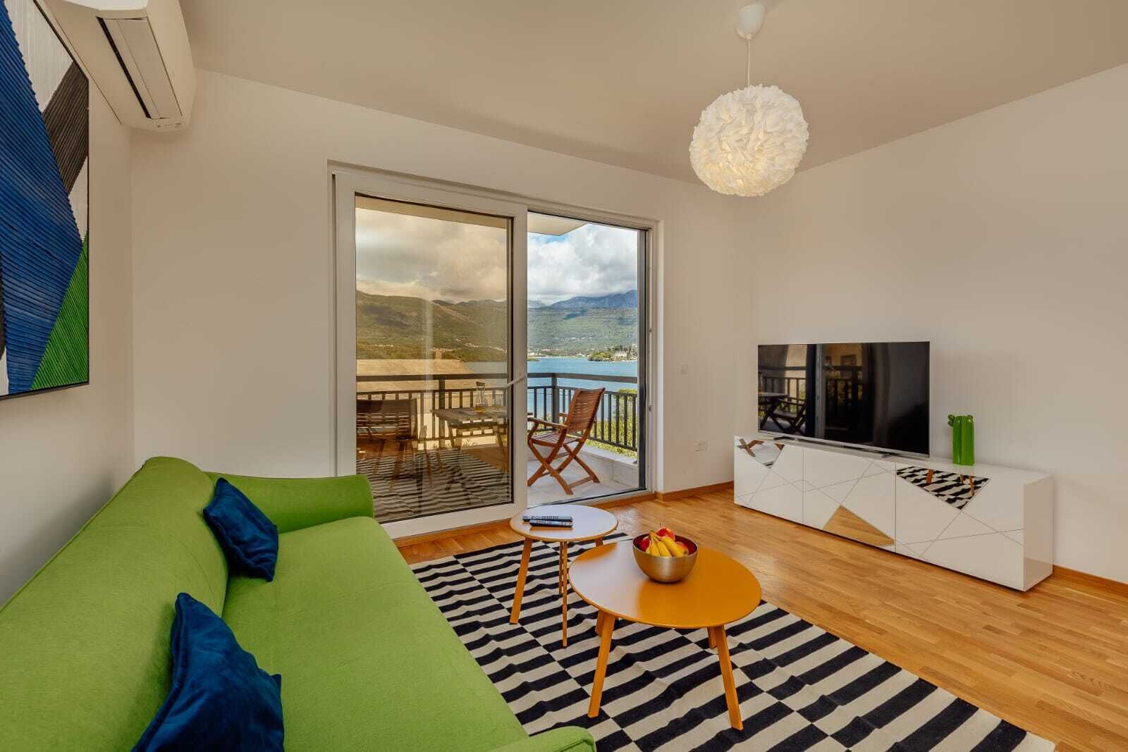 Una sala de estar moderna con un sofá verde, un televisor y un balcón con vistas.