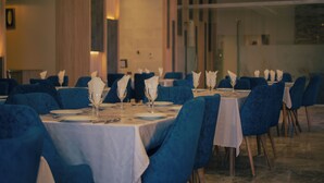 A dining area with tables set for service, blue upholstered chairs, and a neutral color scheme. - Hotel Asslouni (Djelfa)