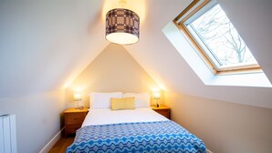 A bedroom with a sloped ceiling, a skylight, a bed with a patterned bedspread, two bedside lamps, and a nightstand.