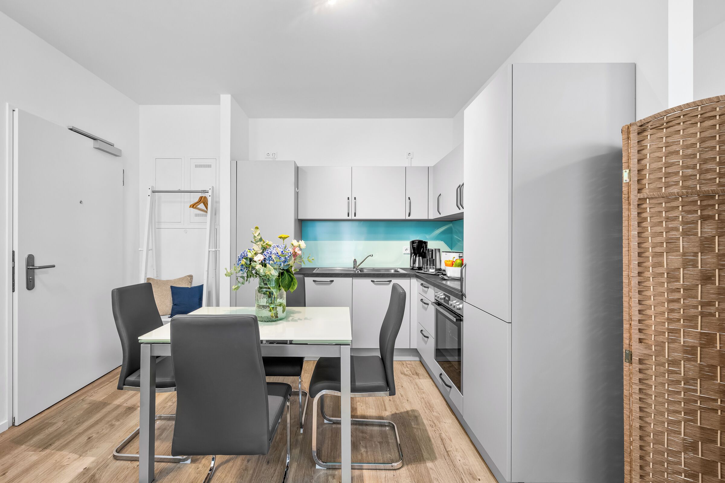 Une cuisine moderne avec des meubles blancs, un îlot central et un coin repas comprenant une table et des chaises.