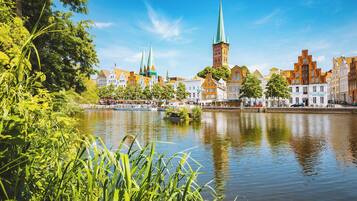 Blick auf den Fluss mit historischen Gebäuden, darunter ein markanter Turm und Zinnen, umgeben von üppigem Grün.