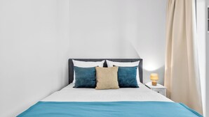 Un letto con materasso bianco, coperta blu e tre cuscini in tonalità di blu e beige.