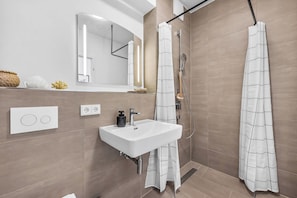 A modern bathroom with a white sink, mirror, and shower curtain. - Modern Apartment Pure Travemünde with Terrace, Parking and Partial Sea View (Lübeck)