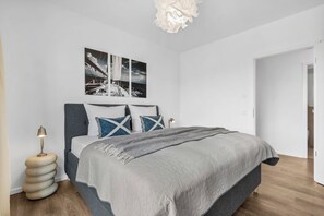 Een moderne slaapkamer met een bed, nachtkastje, lamp en een kunstwerk aan de muur.