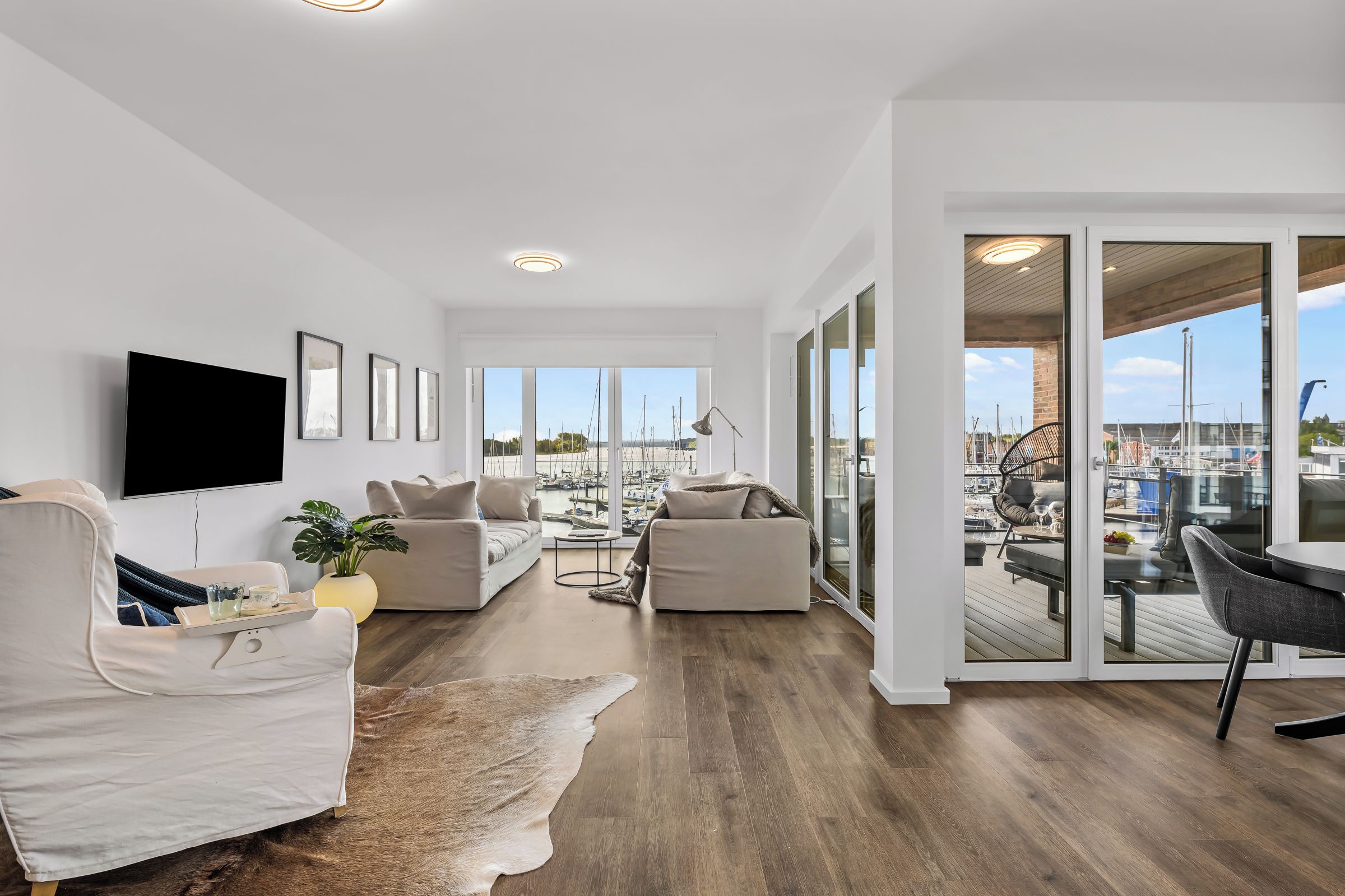 A spacious living area with a large window overlooking a marina, furnished with sofas and a flat-screen TV.