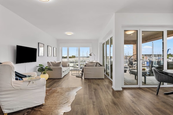 A spacious living area with a large window overlooking a marina, furnished with sofas and a flat-screen TV. - Modern Apartment Pure Travemünde with Terrace, Parking and Partial Sea View (Lübeck)