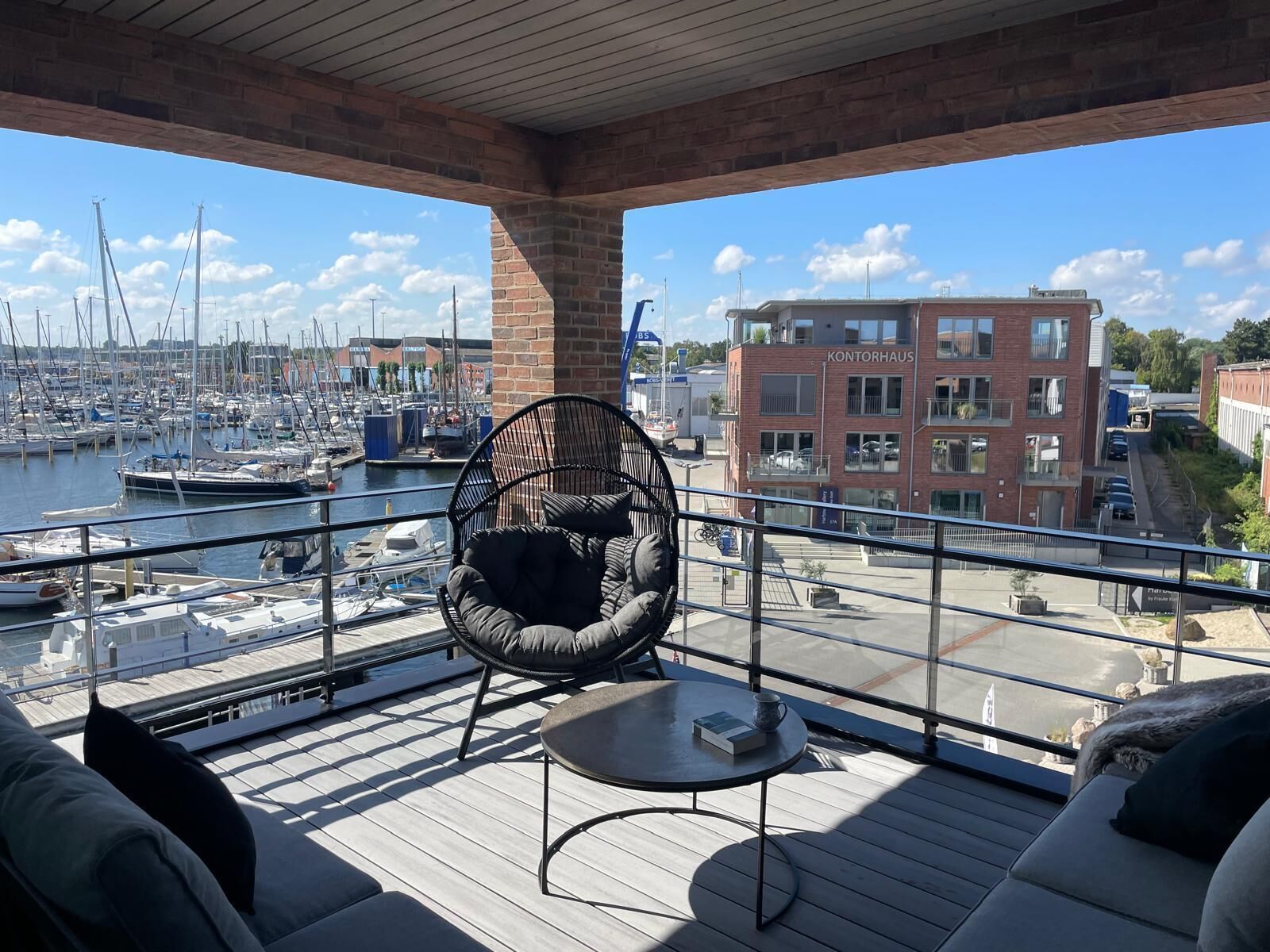 A balcony with a view of a marina, a round chair, and a table with a book.