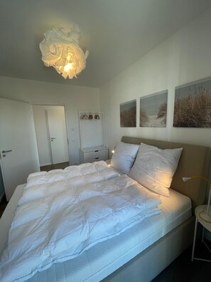A bedroom with a large bed, bedside tables, a wardrobe, and wall art. - Modern Apartment Pure Travemünde with Terrace, Parking and Partial Sea View (Lübeck)