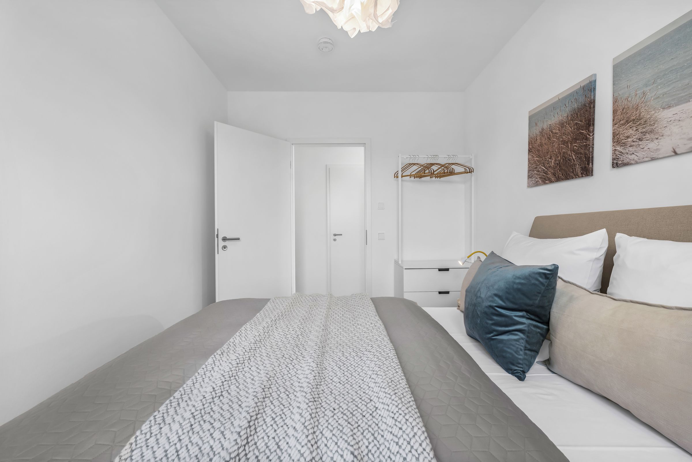 Un dormitorio moderno con cama, mesitas de noche, una puerta y una lámpara fijada a la pared.
