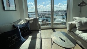 Ein Wohnzimmer mit einer Couch, einem Couchtisch und Blick auf eine Marina durch große Fenster.