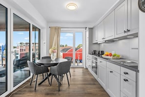 A modern kitchen with a dining area, large windows, and a view of the city. - Modern Apartment Pure Travemünde with Terrace, Parking and Partial Sea View (Lübeck)