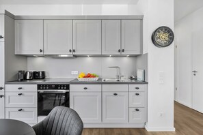 Een moderne keuken met grijze kastjes, een ingebouwde oven en een fruitschaal op het aanrecht.