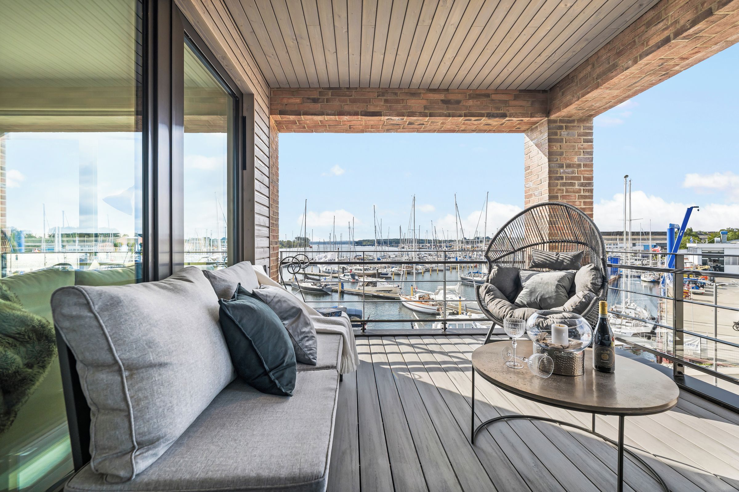 A modern balcony with a sofa and a table, overlooking a marina with boats.