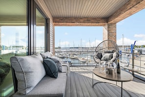 A modern balcony with a sofa and a table, overlooking a marina with boats. - Modern Apartment Pure Travemünde with Terrace, Parking and Partial Sea View (Lübeck)