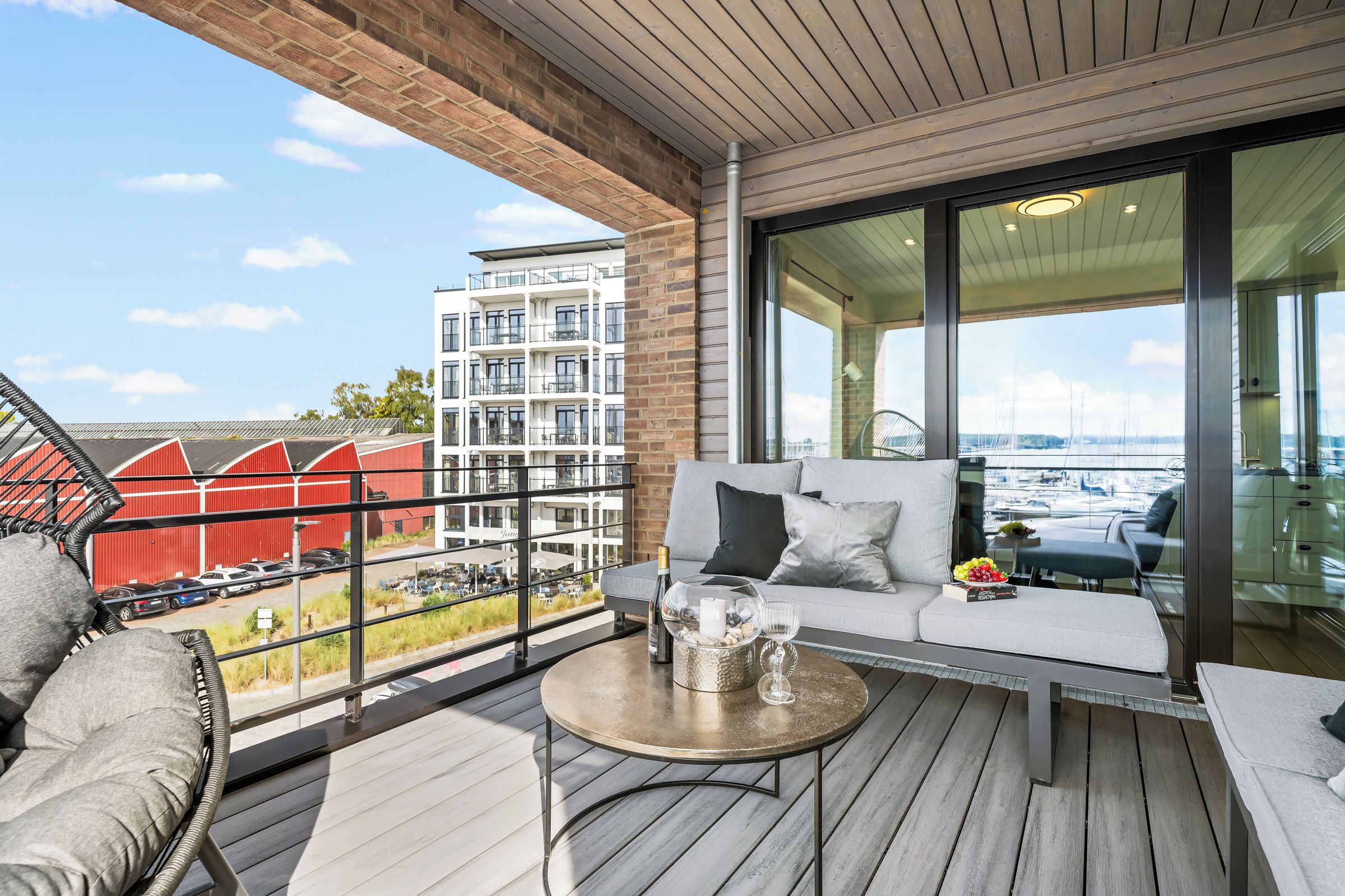 En balkong med en soffa, ett litet bord och utsikt över en byggnad och en småbåtshamn.