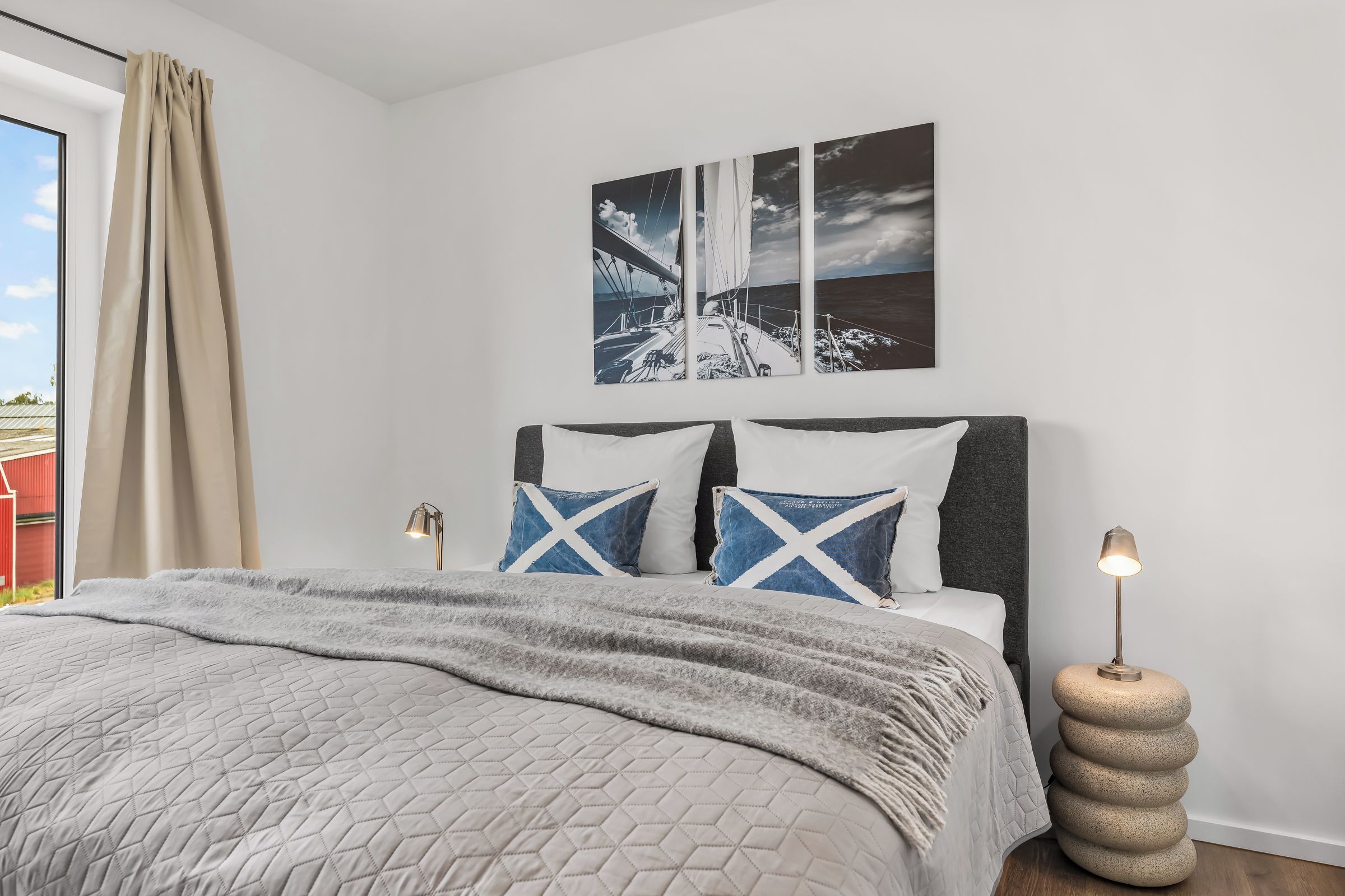 Un dormitorio con cama, cabecera, dos almohadas, una colcha, una obra de arte colgada en la pared, una lámpara de noche y una mesita de noche original.