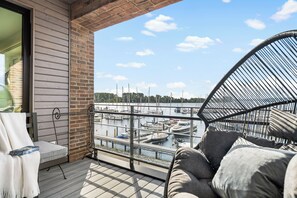 Een balkon met uitzicht op een jachthaven, een rieten stoel en een bank met kussens.