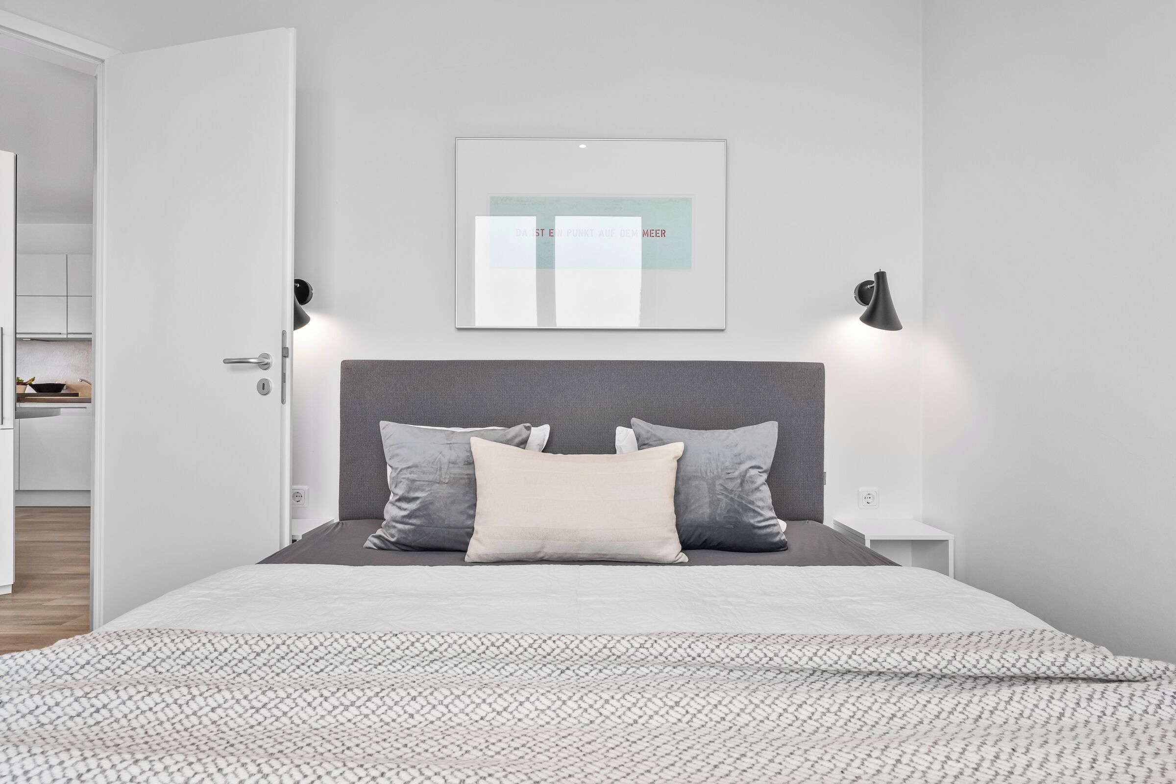 A modern bedroom with a bed, pillows, a bedside table, and a wall-mounted light fixture.