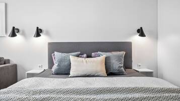 Un dormitorio ordenado con cama, almohadas, mesitas de noche y lámparas de pared.