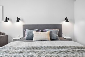 Un dormitorio ordenado con cama, almohadas, mesitas de noche y lámparas de pared.