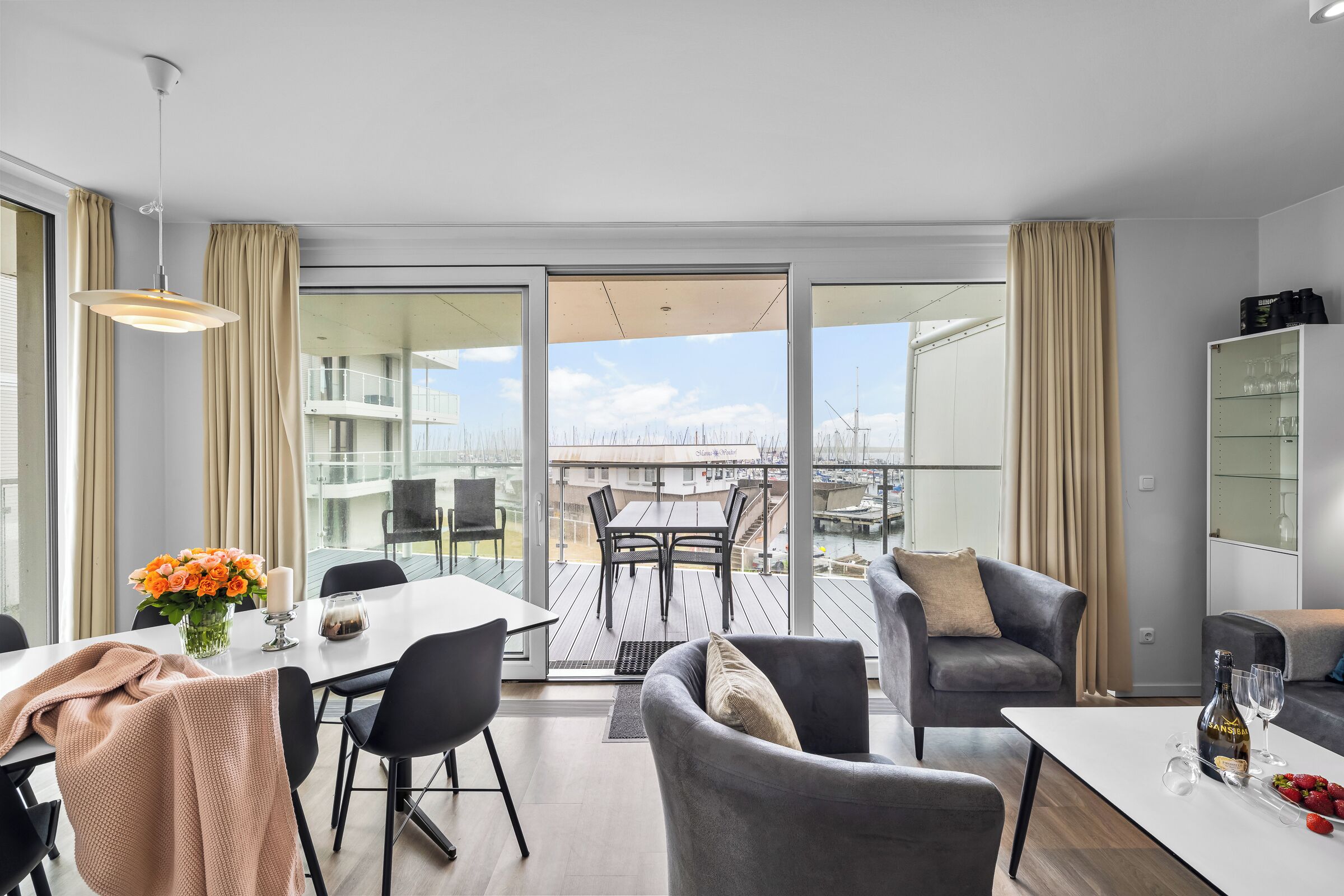 Un salon moderne avec un coin repas, de grandes fenêtres et un balcon aménagé avec du mobilier d’extérieur.